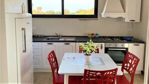 A compact kitchen with white cabinets, a double sink, a stove, and a dining area with a table and red chairs.