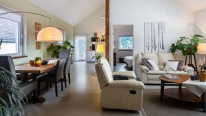 A modern living room with a sofa, a dining table, and chairs. There is a kitchen area in the background with a window. - Snug Apartment in Birresborn With Garden (Birresborn)