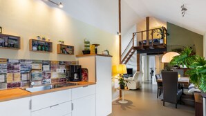 A modern kitchen with white cabinets, a wooden countertop, and a colorful backsplash. There is a dining area with a table and chairs, a lamp, and a staircase leading to an upper level. - Snug Apartment in Birresborn With Garden (Birresborn)