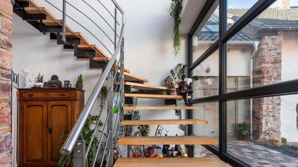 A modern staircase with wooden steps and metal railings, leading to a landing with a wooden table and potted plants. - Snug Apartment in Birresborn With Garden (Birresborn)