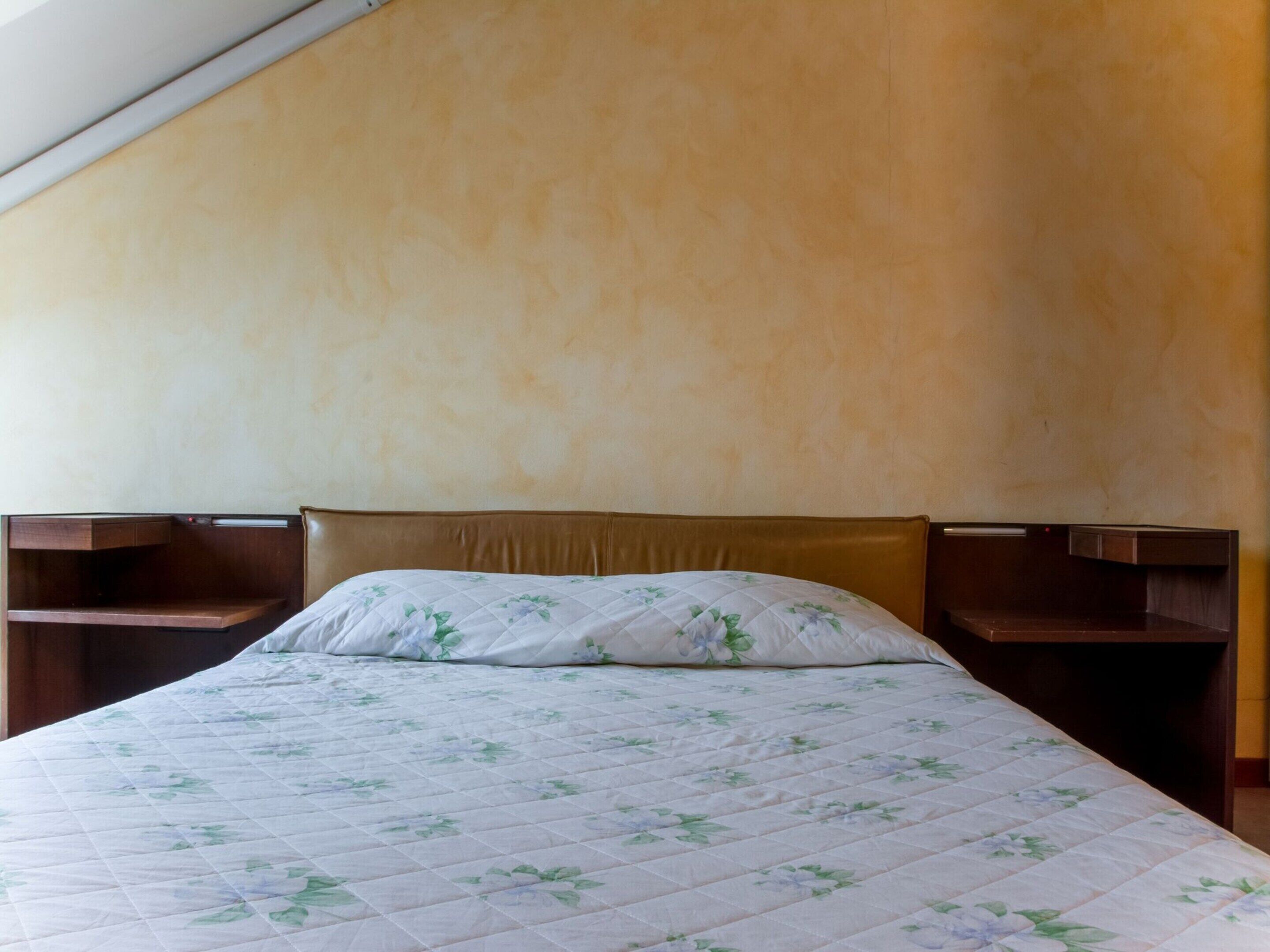 Un lit simple avec une couette à motifs floraux, une tête de lit en bois et des tables de chevet de chaque côté.