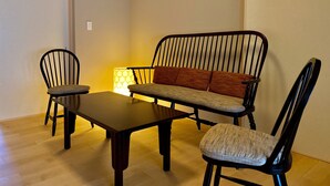 A room with a wooden dining table, two chairs, a sofa, and a lamp. - Campton Higashiyama Roku (Kyoto)