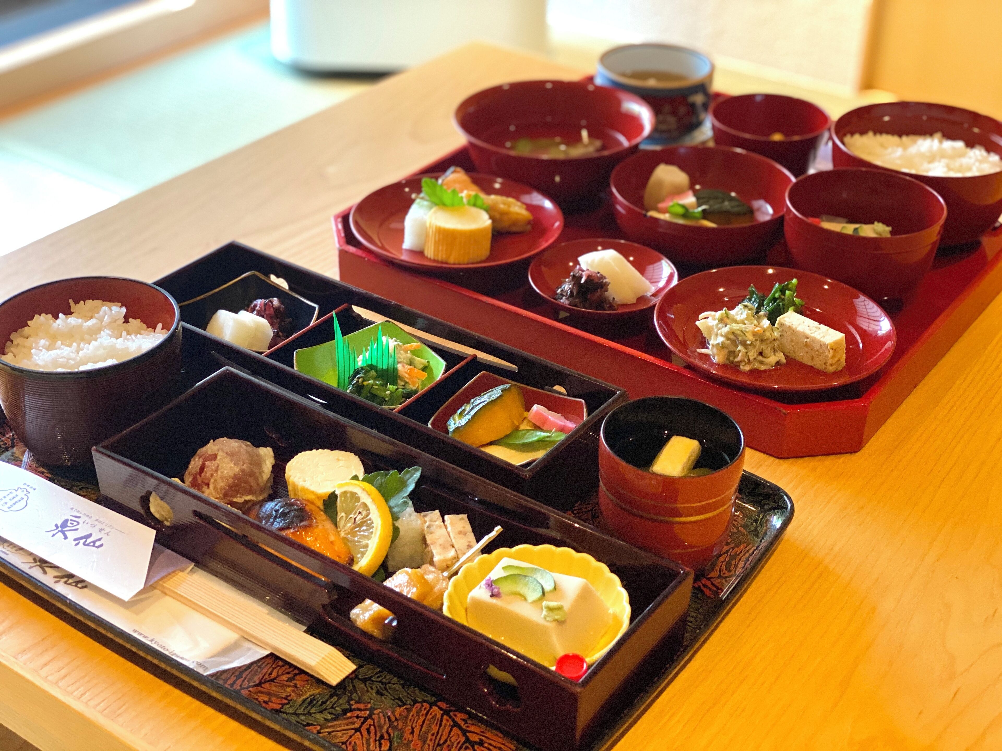 Een traditionele Japanse maaltijdopstelling met diverse gerechten in rode en zwarte kommen, gerangschikt op een dienblad.