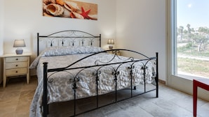 A bedroom with a bed, bedside tables, a window, and a painting on the wall. - Belvilla by OYO Agrivillage San Lorenzo (Noto)