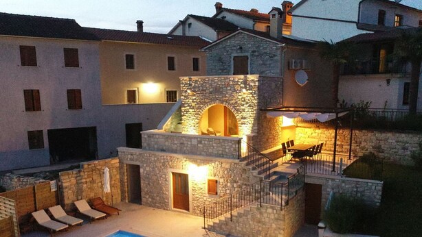A stone building with a pool, outdoor seating, and a staircase leading to an upper level.