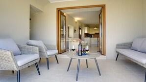 A modern living room with wicker furniture, a round table, and a view into the kitchen.