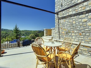 A balcony with wicker chairs and a table, overlooking a stone wall and a forested area. - Holiday Home Pazin With Scenic Pool (Pazin)
