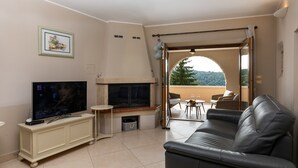 A living room with a TV, fireplace, and a leather sofa. There is a balcony with outdoor seating.