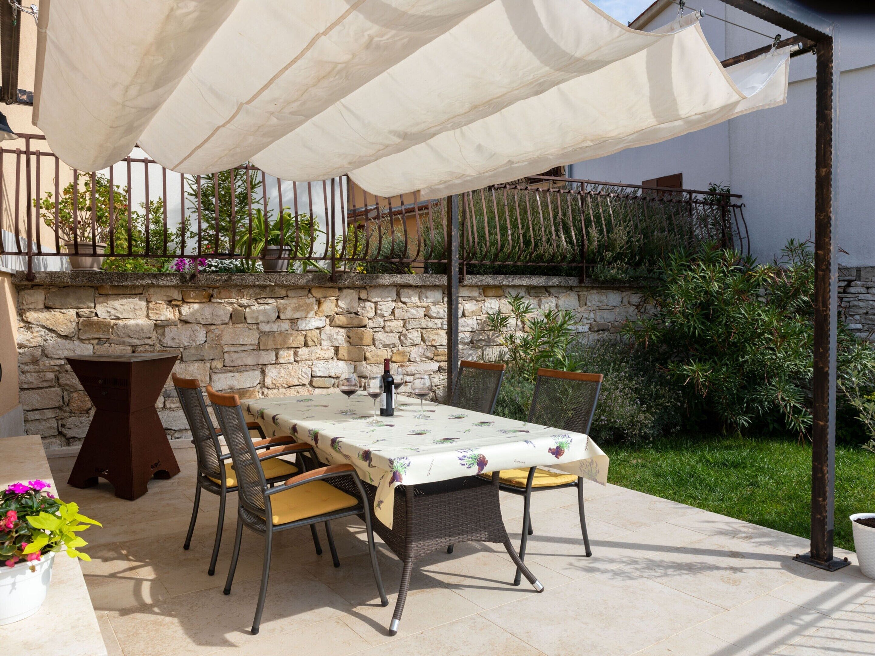 An outdoor patio with a table set for dining, surrounded by chairs and a wine bottle.