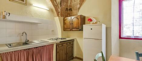 Una cocina con techo abovedado de piedra, un refrigerador blanco, armarios de madera y un ventanal con marco rosa.
