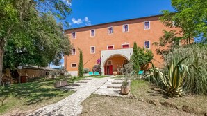 A building with a stone pathway leading to a red door, surrounded by greenery and potted plants. - Tuscan Farmhouse in Montescudaio near Sea (Montescudaio)
