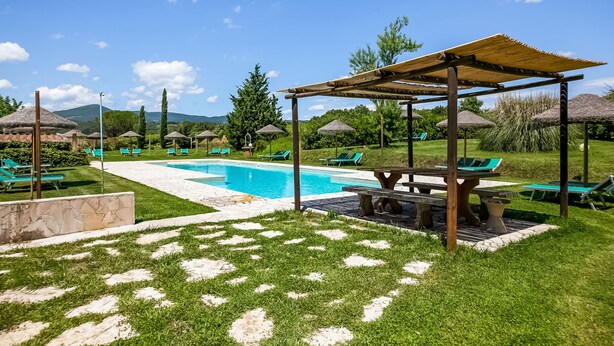 A pool area with a clear blue pool, green lounge chairs, and a pergola structure. - Tuscan Farmhouse in Montescudaio near Sea (Montescudaio)