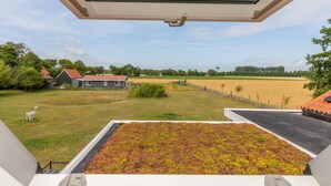 En utsikt från ett fönster med utsikt över en grön äng, ett litet hus och ett inhägnat område.