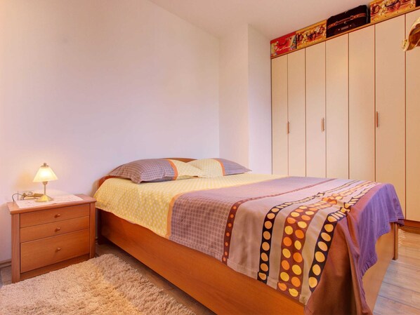 Un dormitorio con cama, mesita de noche, lámpara, armario y alfombra.