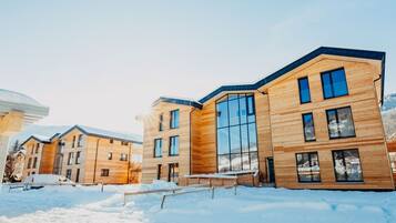 A modern multi-story building with large windows and a wooden facade, surrounded by snow.