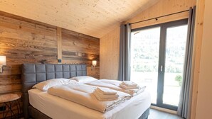 Ein modernes Schlafzimmer mit einem Holz-Kopfteil, einem großen Bett mit weißen Leinen, einem Nachttisch mit Lampe und Blick ins Freie durch eine Schiebetür.