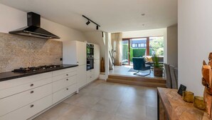 A modern kitchen with white cabinetry, a black range hood, and a large island. - Attractive Holiday Home, Sunny Garden, Near the Beach (Nieuwvliet)