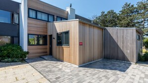 A modern building with a wooden facade, a small attached structure, and a paved entrance area. - Attractive Holiday Home, Sunny Garden, Near the Beach (Nieuwvliet)