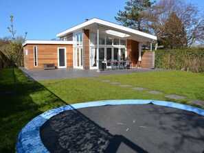 A modern two-story house with a large glass window area and a patio with outdoor furniture.