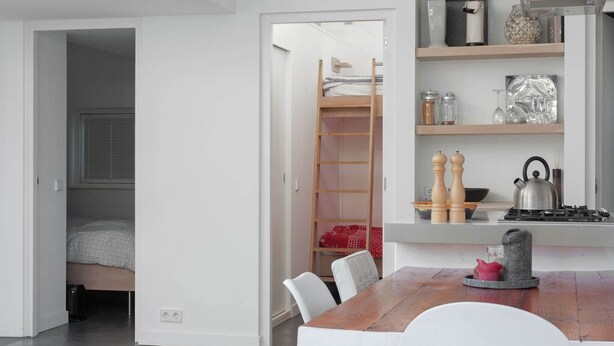 A modern kitchen with a wooden dining table, white chairs, and a built-in stove. There is a ladder leading to a loft bed in the adjacent room. - Family Home Near Sea & Dunes (Noordwijk)