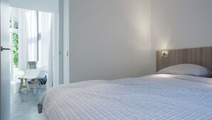 A bedroom with a large bed, a wooden headboard, and a nightstand with a lamp. There is a window with curtains and a view of greenery outside. - Family Home Near Sea & Dunes (Noordwijk)