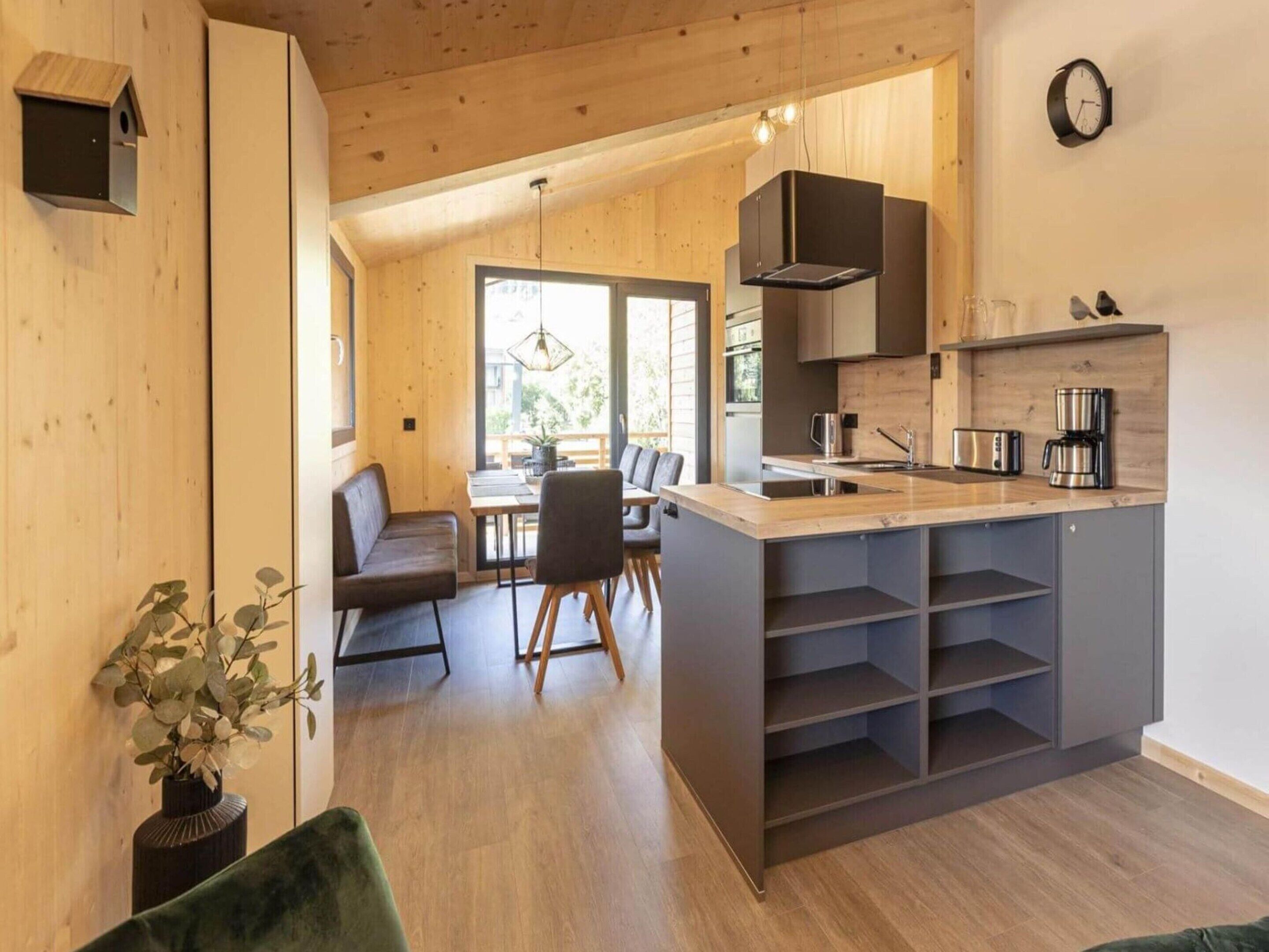 A modern kitchen with a central island, wooden flooring, and a view to an outdoor area.