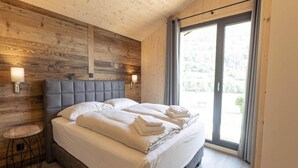 A bedroom with a wooden headboard, a large bed with white linens, a bedside table, and a view through a glass door. - Apartment With Balcony (Sankt Georgen am Kreischberg)