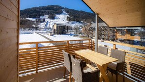 A wooden deck with a table and chairs, overlooking a snowy landscape with buildings and a mountain. - Apartment With Balcony (Sankt Georgen am Kreischberg)