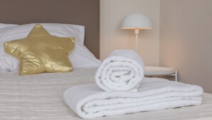 A neatly made bed with a star-shaped pillow, a rolled white towel, and a white lamp on a bedside table. - Holiday Apartment in a Prime Location on the Veerse Lake (Arnemuiden)