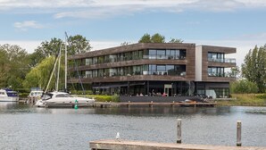 A modern multi-story building with a dock and boats, featuring outdoor seating and a view of the water. - Holiday Apartment in a Prime Location on the Veerse Lake (Arnemuiden)
