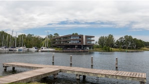 A modern building with a dock extending into a calm lake, surrounded by trees and boats. - Holiday Apartment in a Prime Location on the Veerse Lake (Arnemuiden)