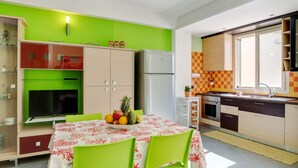 Uma cozinha moderna com parede verde, uma mesa de jantar com cadeiras e uma fruteira.