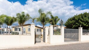 Uma área residencial murada com uma estrada pavimentada, céu claro e palmeiras.