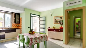 Cozinha luminosa com uma mesa de jantar posta para dois, uma tigela de frutas e um armário com um vaso.