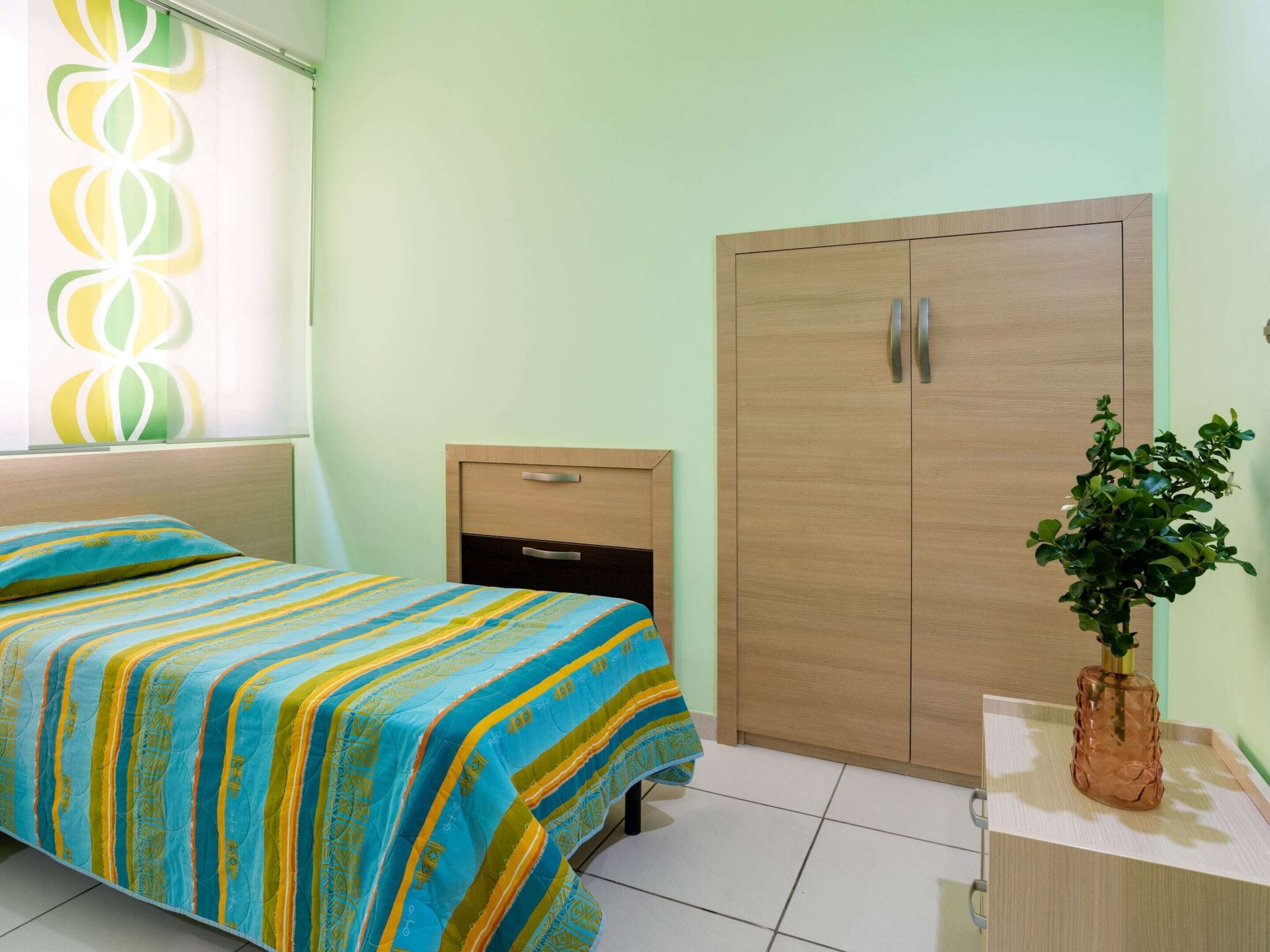 Un dormitorio con cama, mesita de noche, armario y planta en maceta.