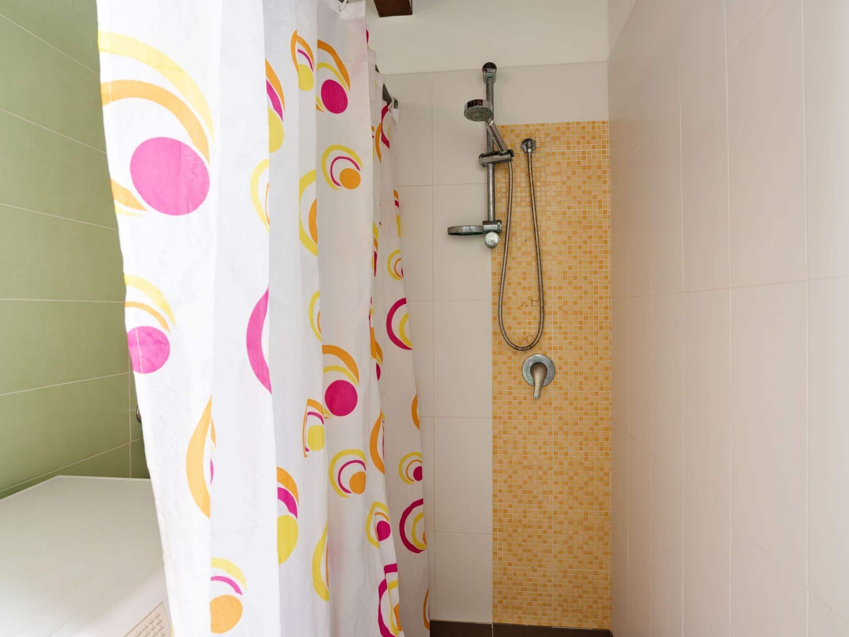A bathroom with a shower, a colorful curtain, and tiled walls.