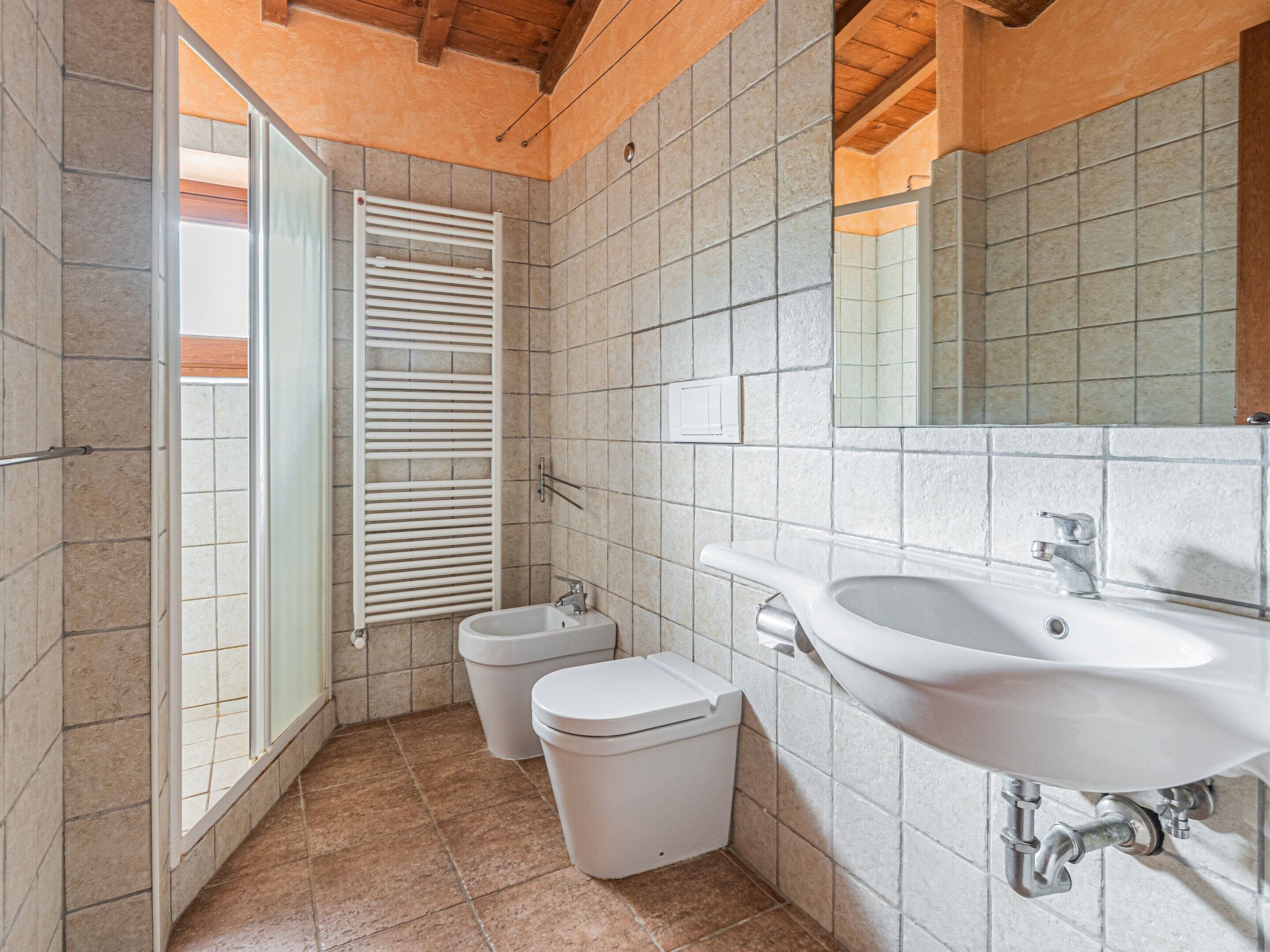 A bathroom with a sink, toilet, bidet, and a window with blinds.