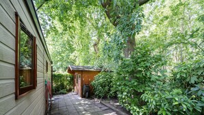 A narrow stone pathway leading to a wooden shed with a wheelbarrow, surrounded by lush greenery. - Pleasing Chalet in Stegeren near Forest (Stegeren)