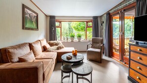 A living room with a sofa, armchair, coffee table, and TV stand. - Pleasing Chalet in Stegeren near Forest (Stegeren)
