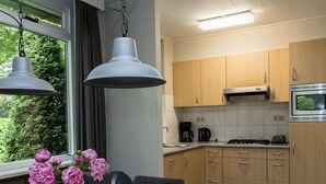 Moderni keittiö, jossa on puukalusteet, kaasuliesi ja sisäänrakennettu uuni. Keittiössä on ruokapöytä tuoleineen ja maljakko, jossa on kukkia.