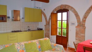 A cozy room with a sofa, a table, and a kitchen area with yellow cabinets and a brick archway. - Belvilla by OYO Nando (Asciano)