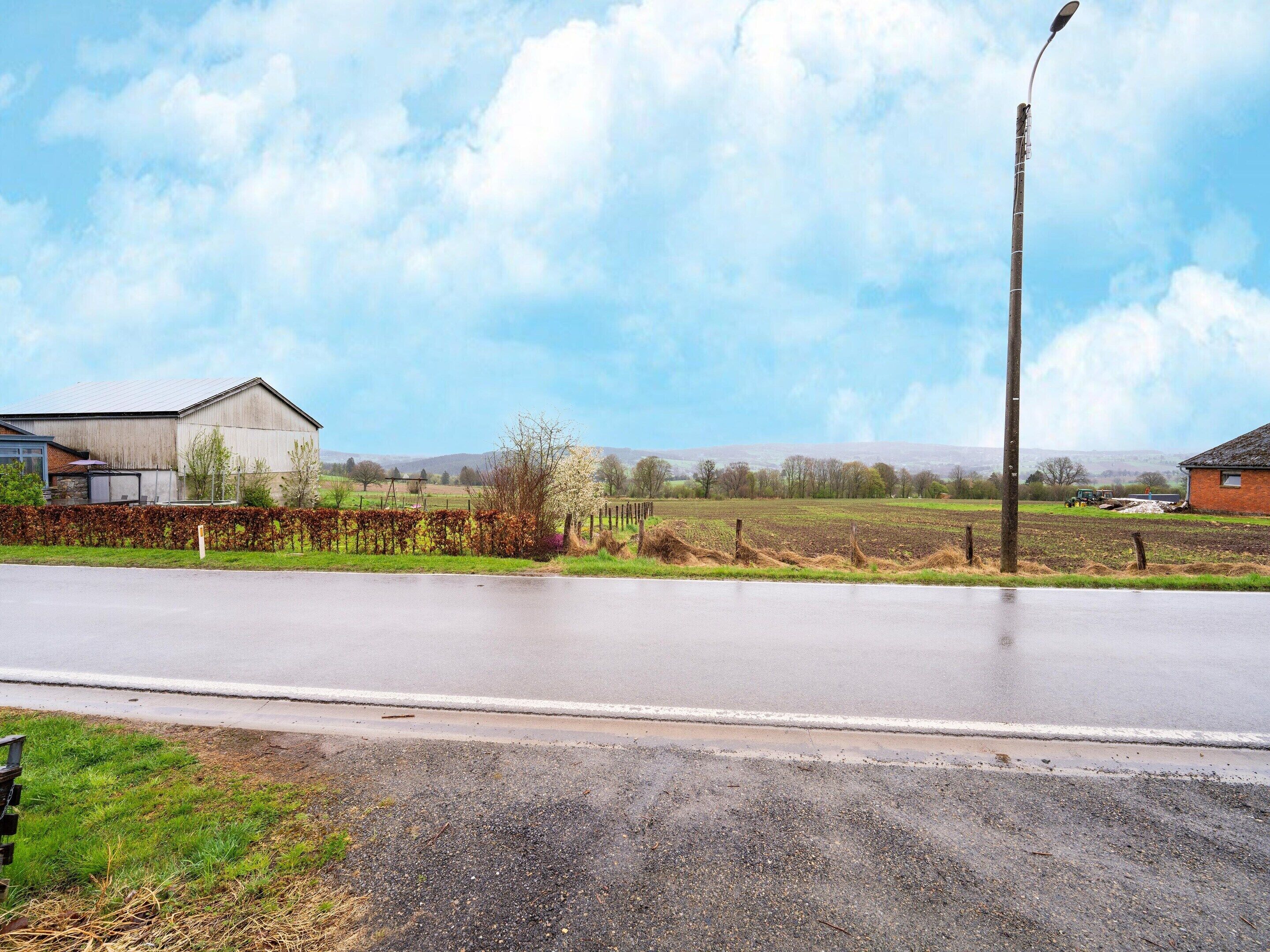 A rural road with a metal fence, a building, and fields in the background.