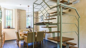 Un comedor con mesa y sillas, una escalera de madera y una ventana con cortinas.