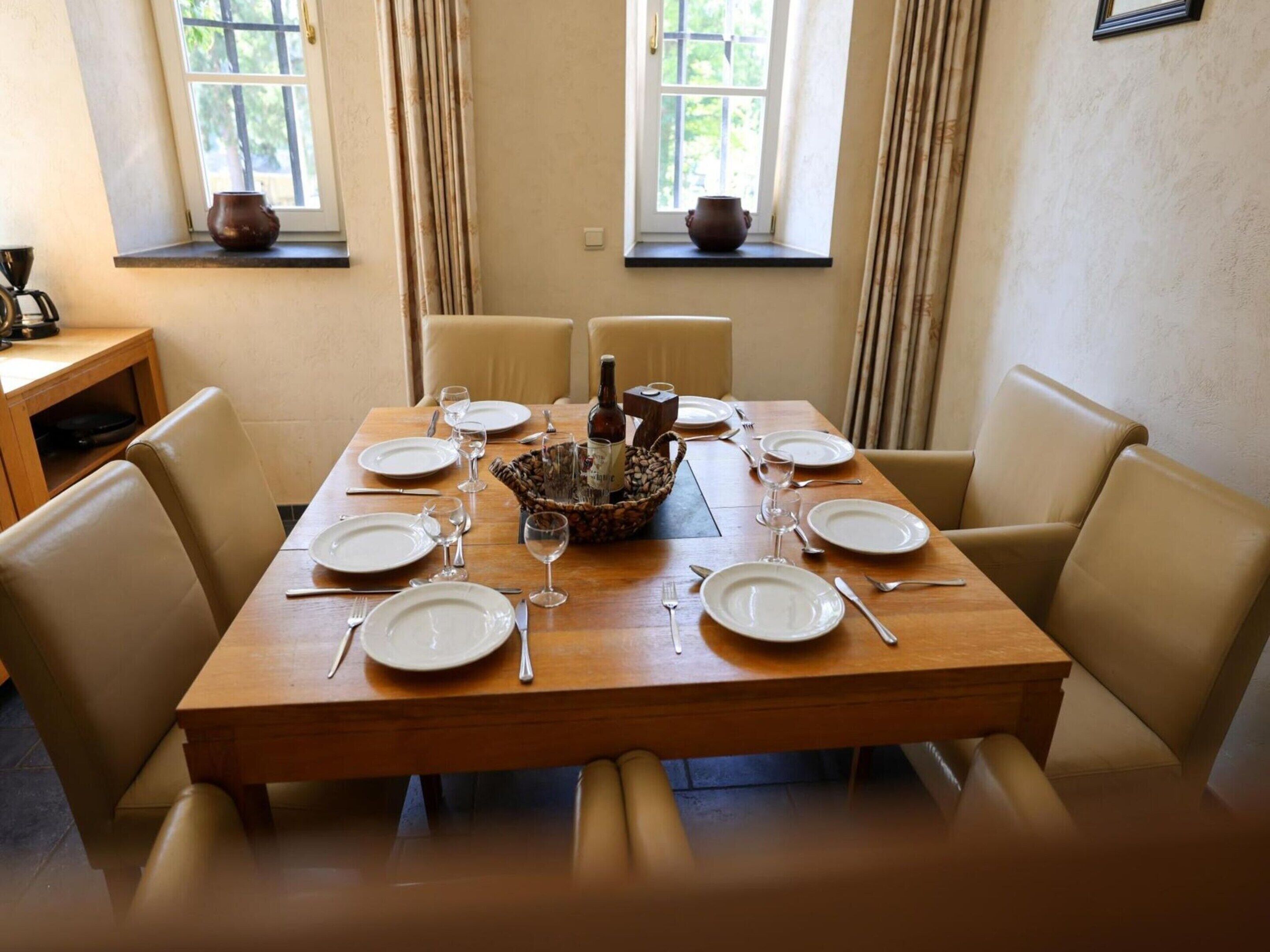 A dining table set for six with chairs, a basket of bread, and a bottle of wine.