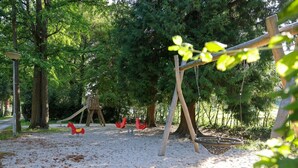 Un parque infantil con columpios, un tobogán y una estructura para escalar, rodeado de árboles.