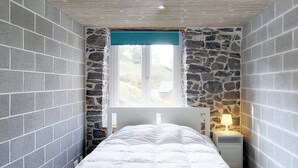 Quarto com parede de pedra decorativa, cama branca e mesa de cabeceira com abajur.