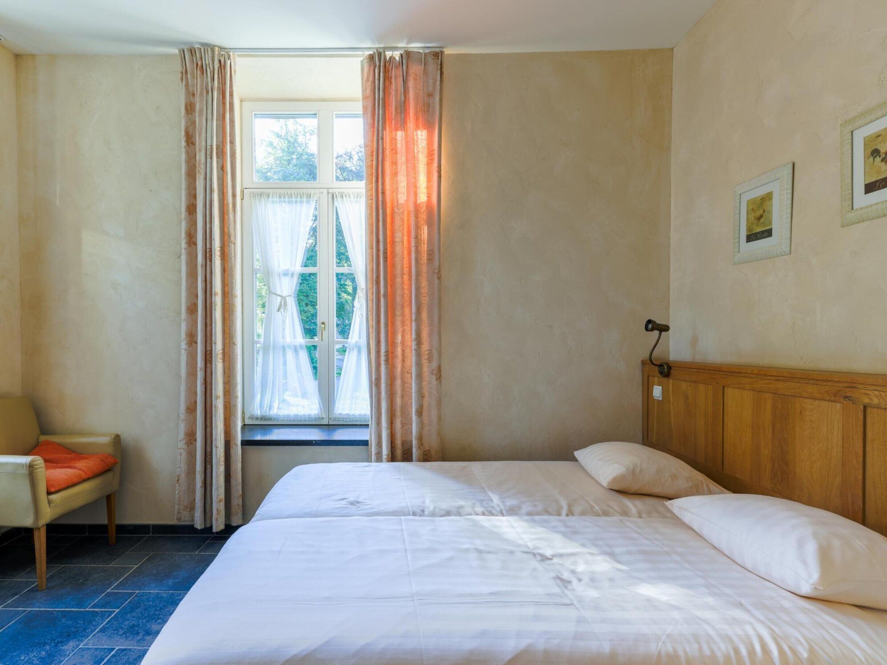 A hotel room with a large bed, a chair, a window with curtains, and a wooden headboard.