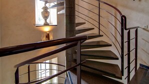 Un escalier en colimaçon avec une rampe en métal, une colonne en pierre et une fenêtre ornée d’un vase.