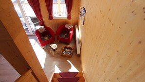 A wooden interior with two red armchairs, a small round table, and a window with red curtains.