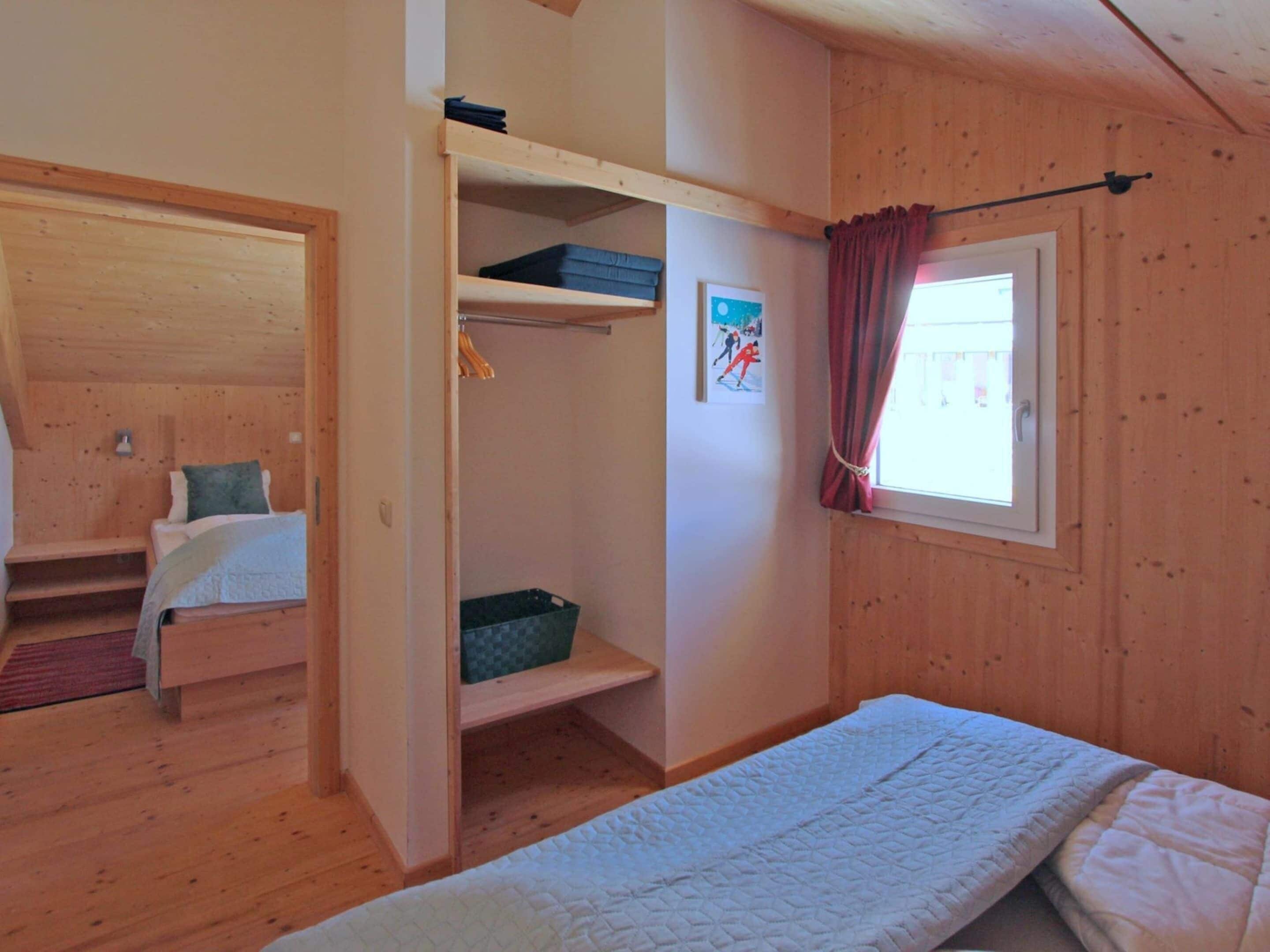 A small, cozy room with a bed, a wooden wardrobe, and a window with curtains.